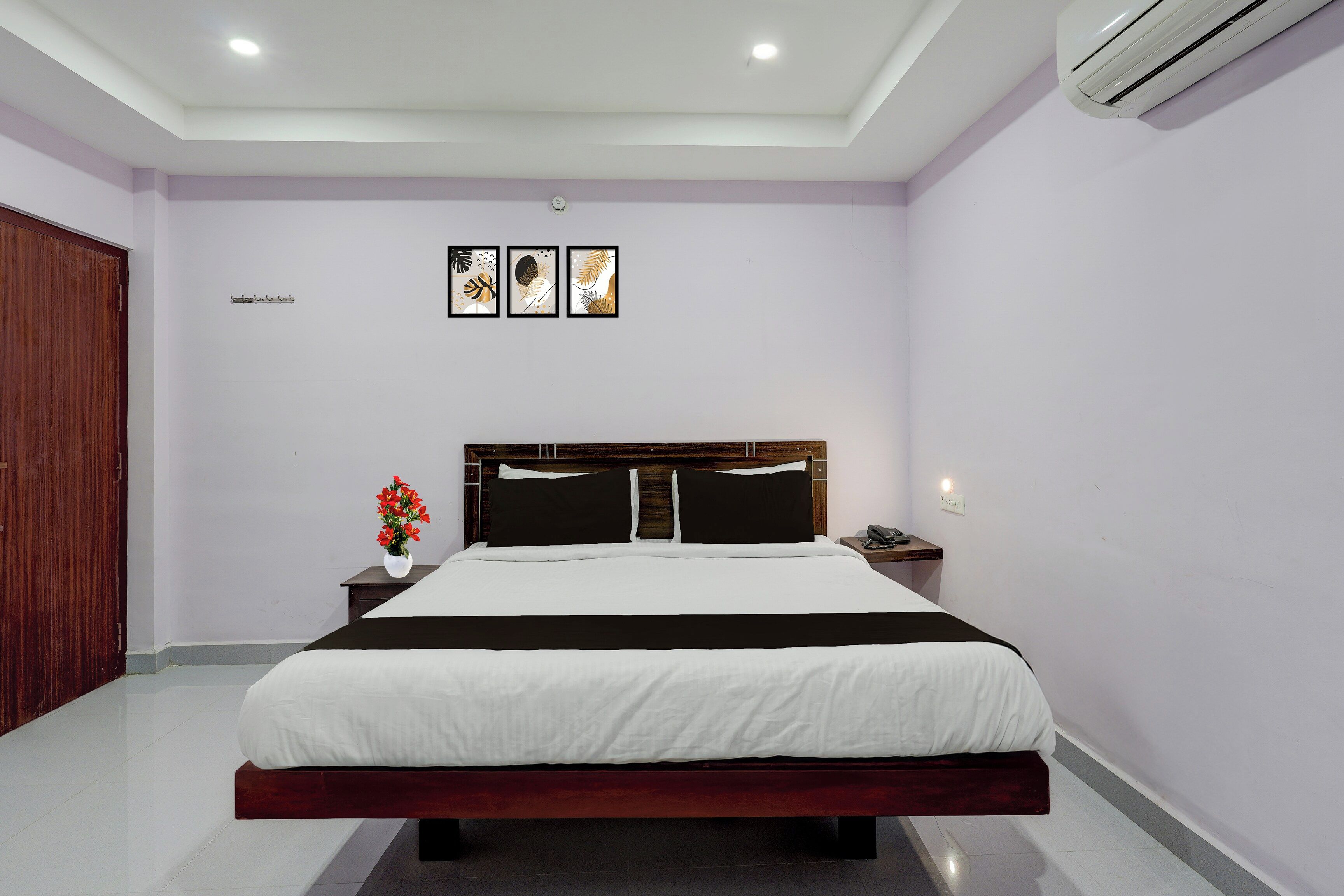 Un dormitorio con cama, mesita de noche y velador con un teléfono.