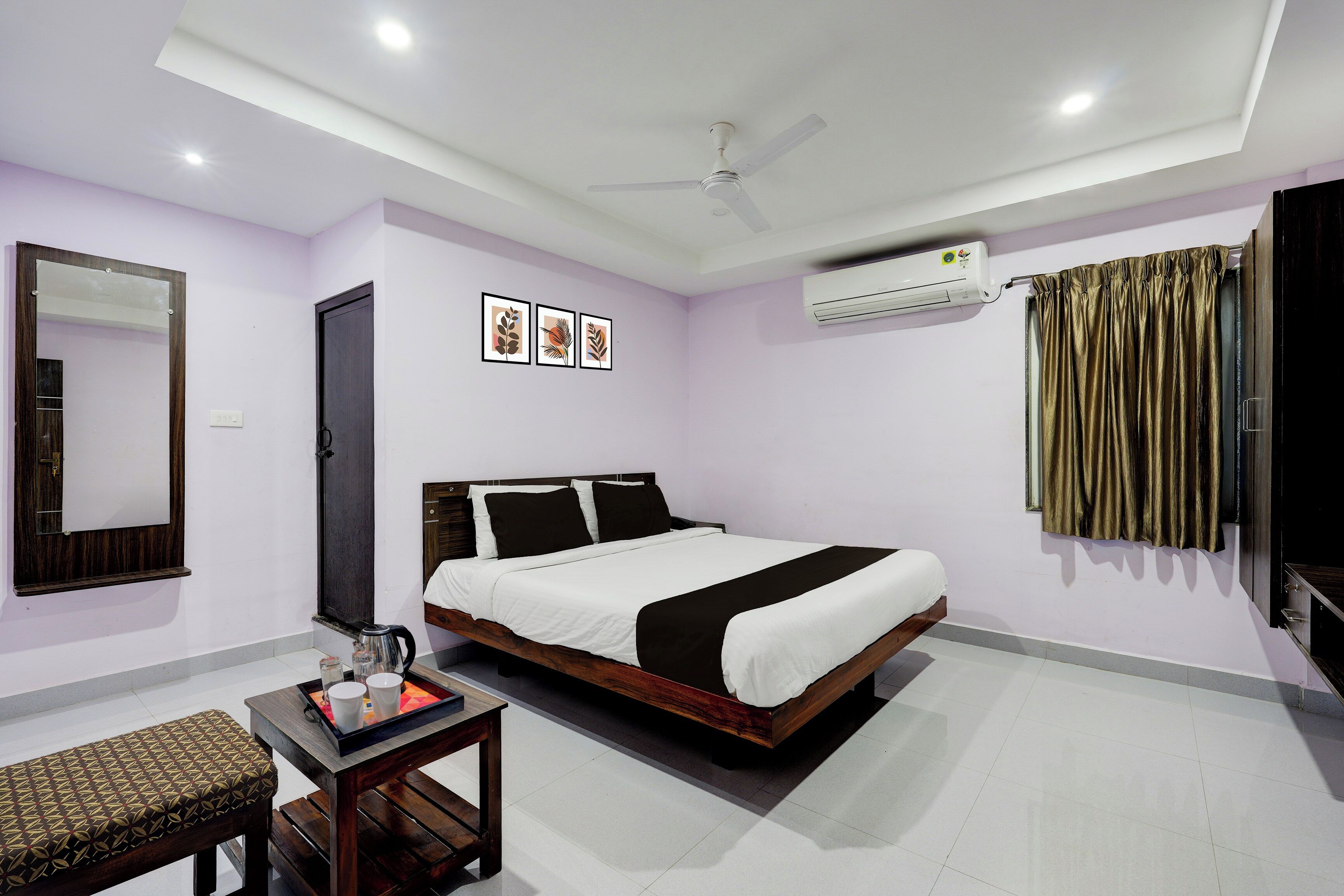 Un dormitorio con cama, mesita de noche, espejo, decoración en la pared, equipo de aire acondicionado y ventana con cortinas.
