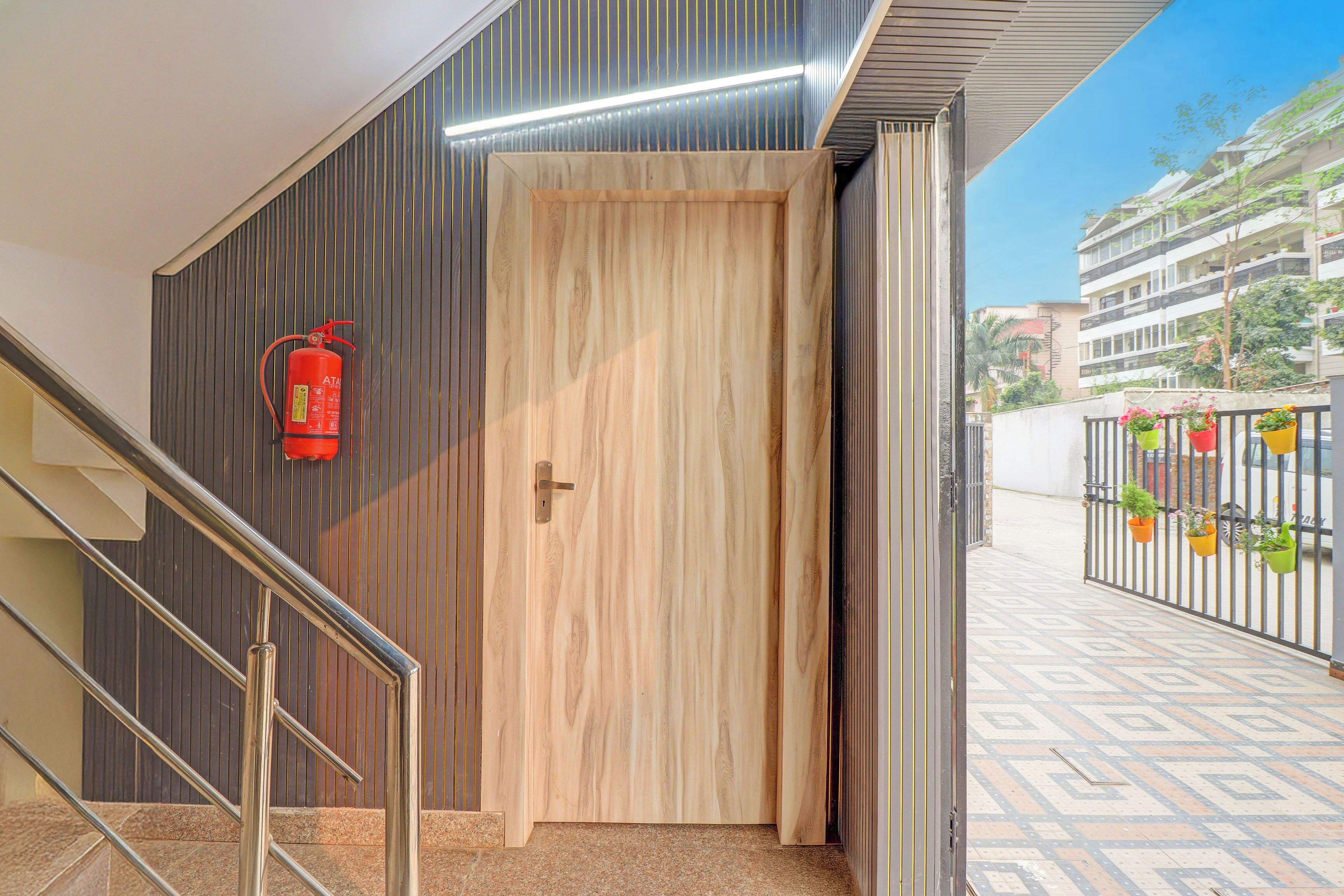 Una puerta de madera con manija metálica, un extintor fijo en la pared y una escalera con barandillas de metal.