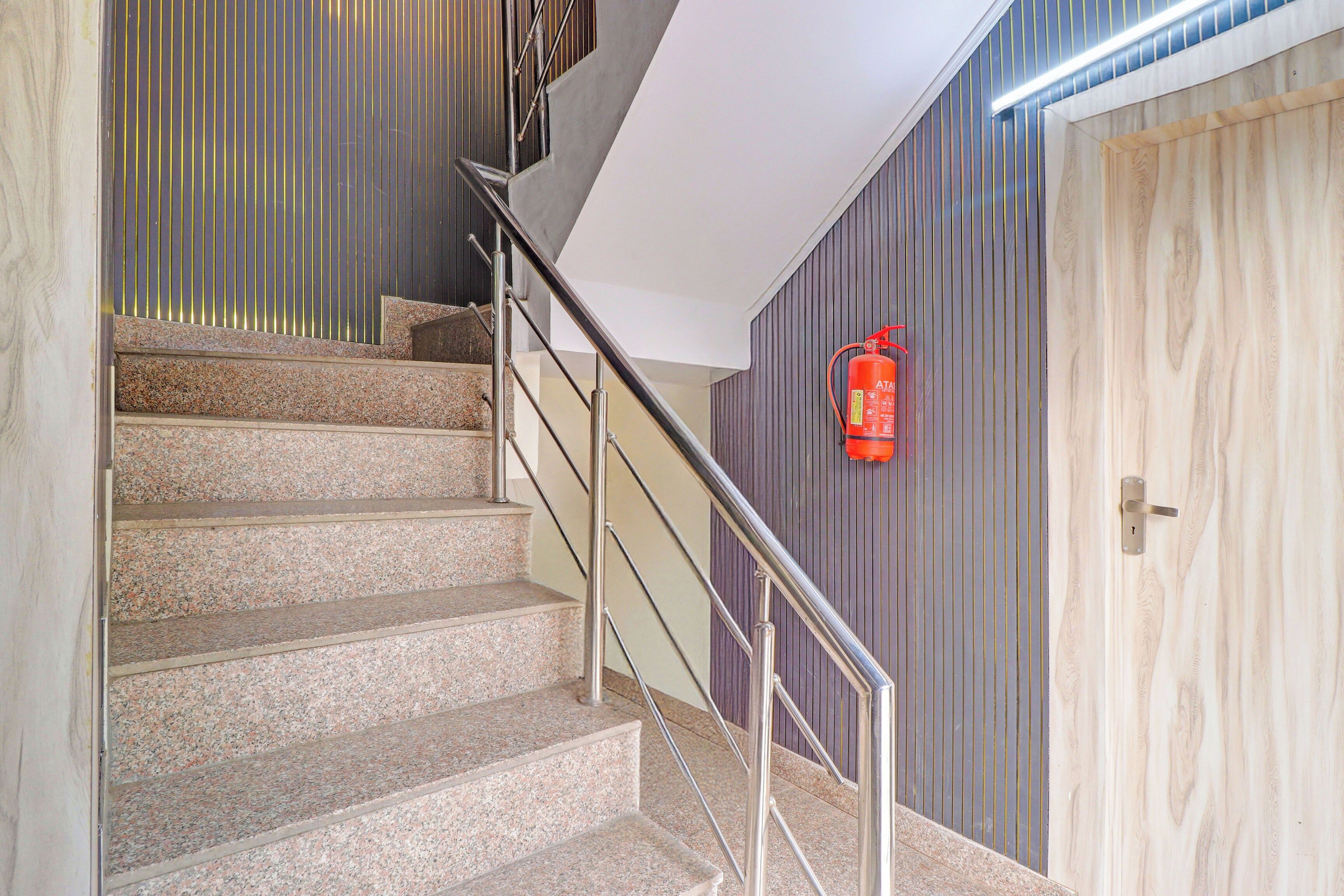 Una escalera con escalones de granito y barandillas metálicas, que conduce a una habitación con una puerta de madera y un extintor colgado en la pared.