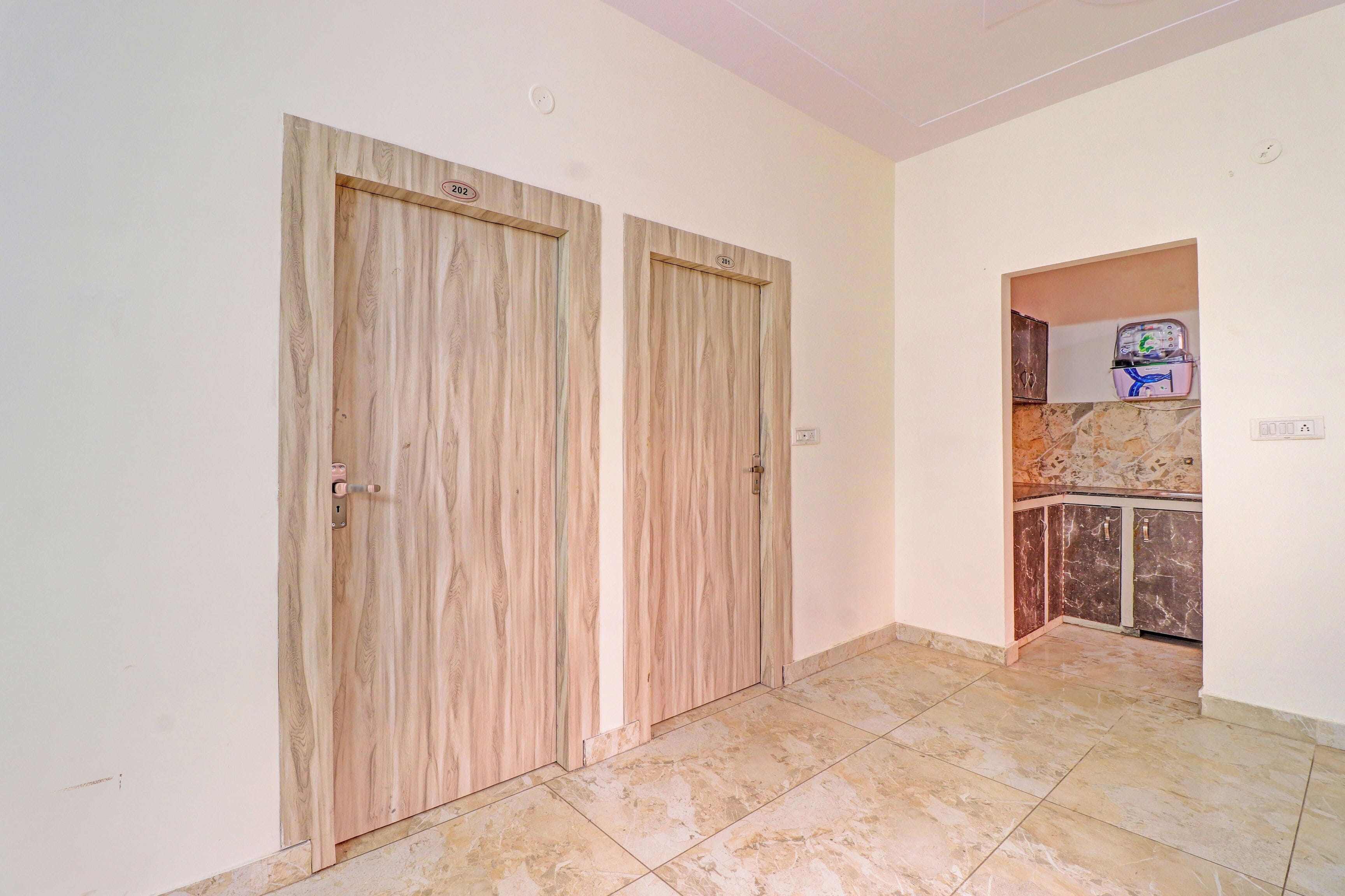 Un pasillo con dos puertas de madera, piso de baldosas de mármol y una zona de cocina con armarios y encimera.