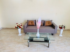 A living room with a glass coffee table, a sofa with cushions, and two vases with flowers. - Hotel O Manglam Hotel (Lucknow)