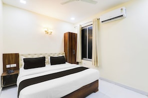 A hotel room with a bed, bedside table, lamp, wardrobe, window, and air conditioning unit. - Hotel O Manglam Hotel (Lucknow)