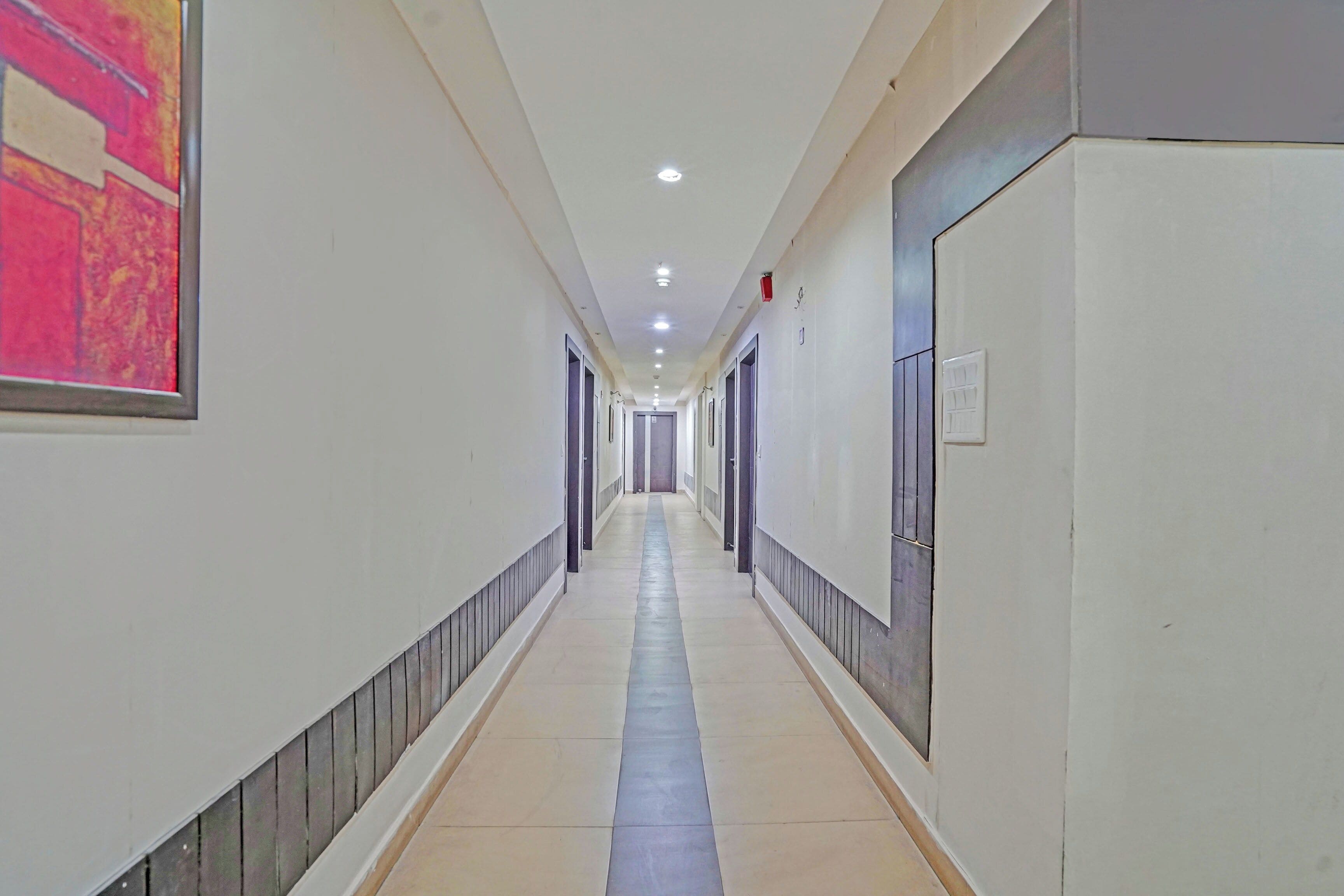 A long, narrow hallway with doors on both sides, recessed lighting, and a tiled floor.