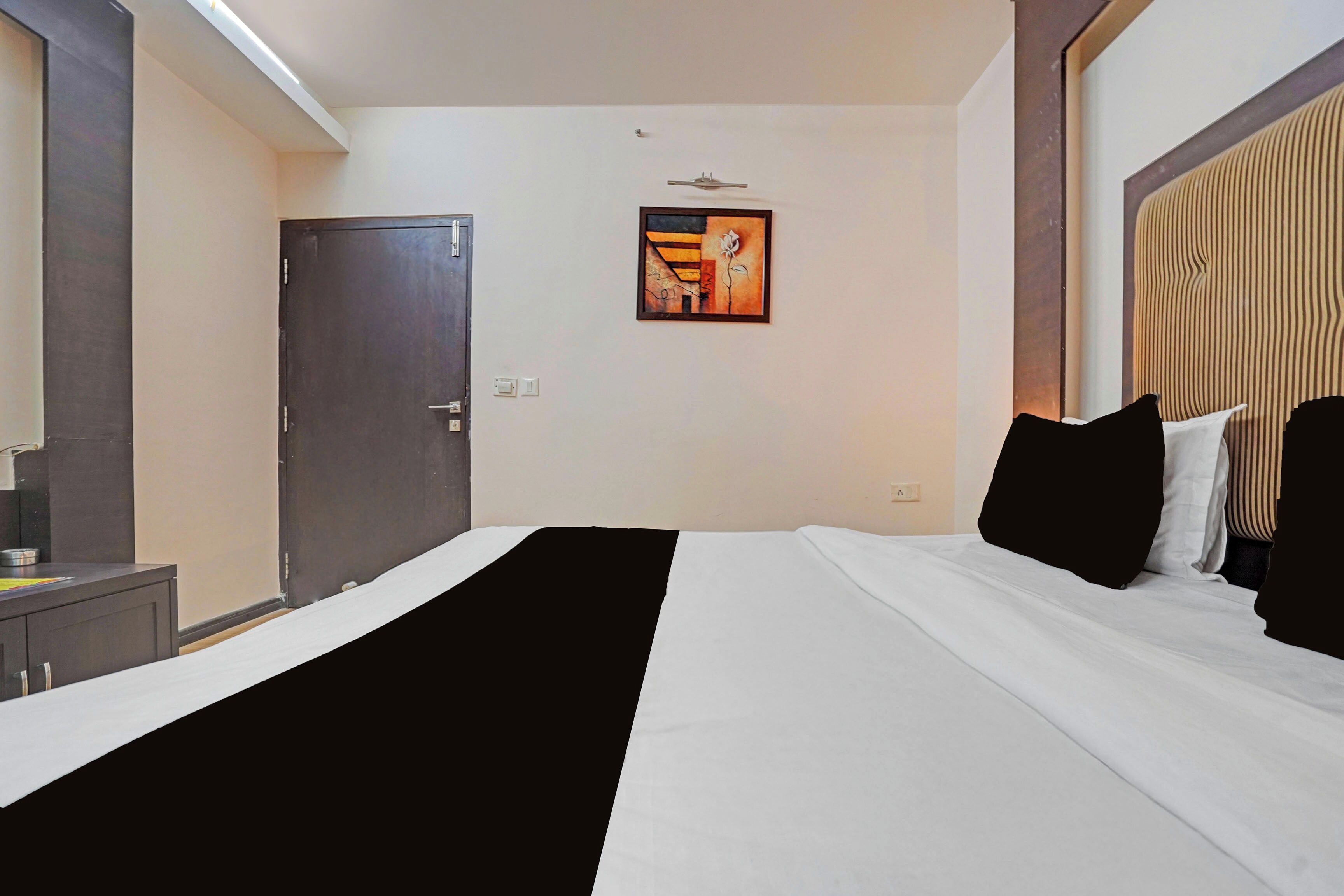A hotel room with a bed, a door, a wall-mounted light, and a painting.