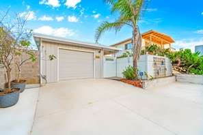 A residential property with a garage, a covered porch, and a landscaped front yard with a palm tree. - Steps To Beach, Perfect For Families, W/Jacuzzi! (Oxnard)