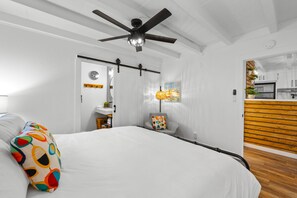 A bedroom with a bed, a ceiling fan, a bedside table, a nightstand, and a window with a view of the outside. - Steps To Beach, Perfect For Families, W/Jacuzzi! (Oxnard)