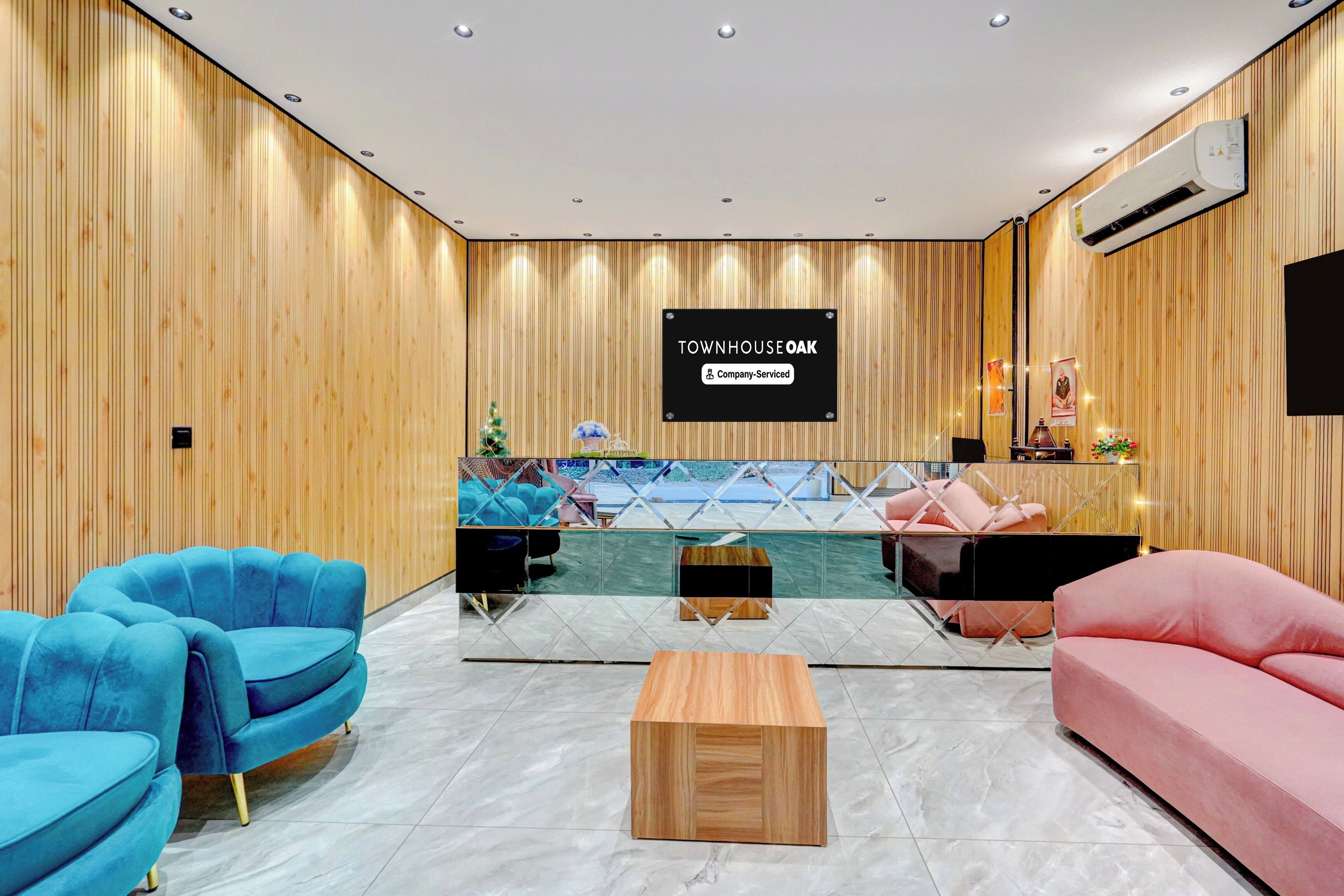 Una moderna zona de recepción con un panel de madera, mostrador de recepción y áreas de descanso con sofás azules y rosados.