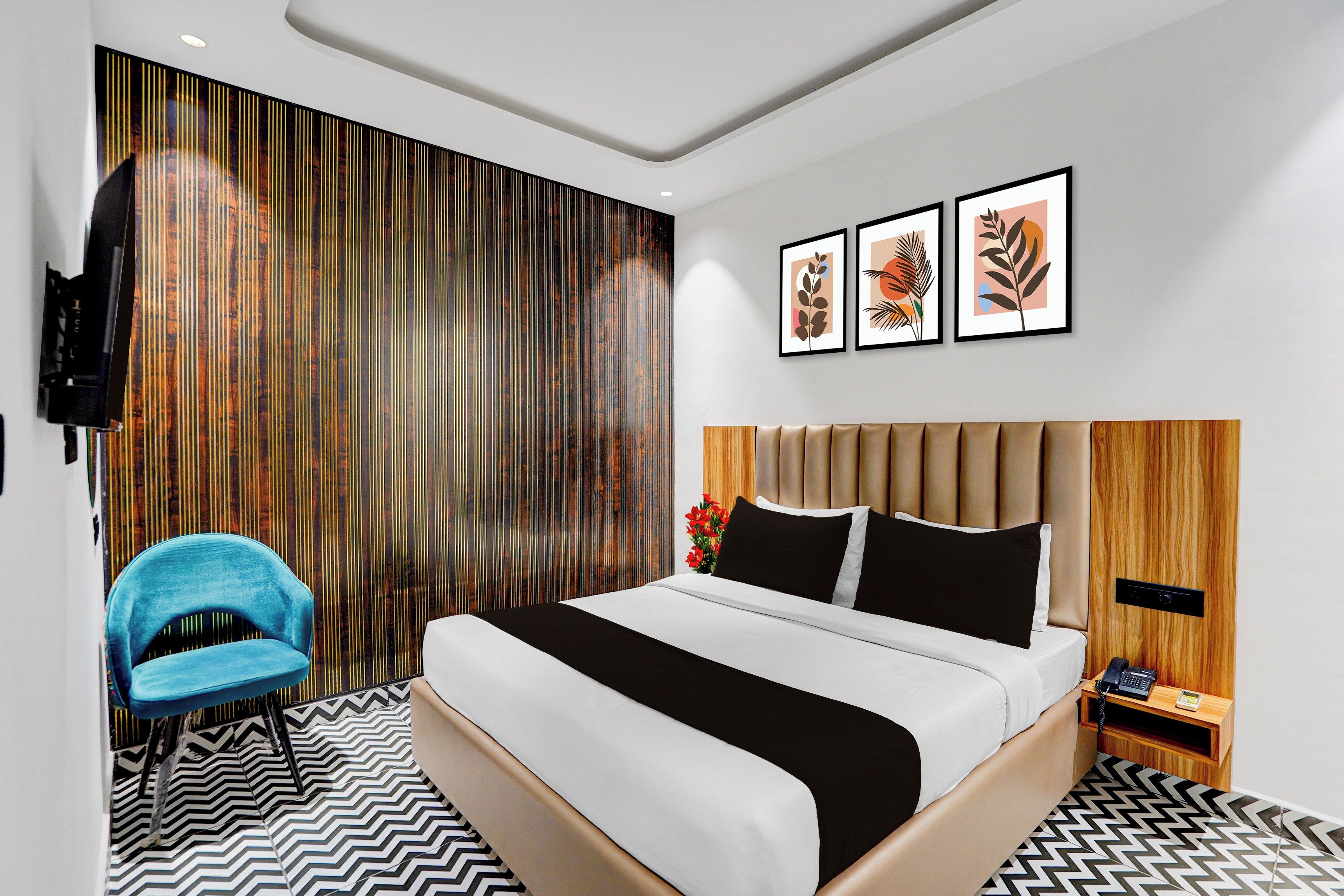 Una habitación de hotel moderna con una cama grande, una silla azul, un cabecero de madera y tres obras de arte enmarcadas en la pared.
