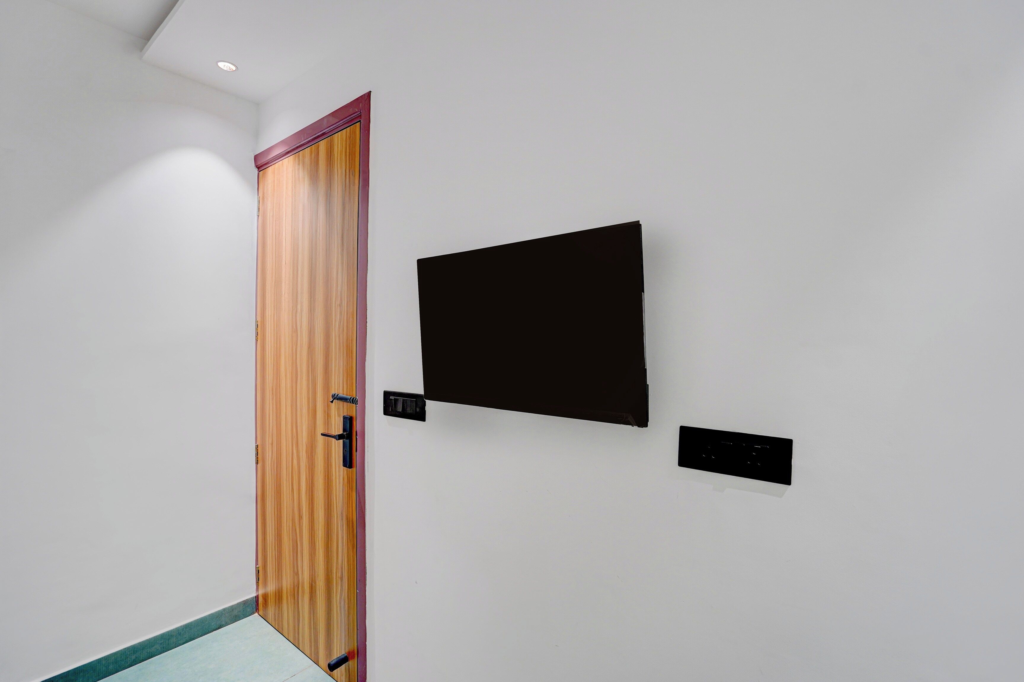 Un pasillo con una puerta de madera, un objeto negro fijado a la pared y un panel negro pequeño.
