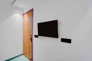 Un pasillo con una puerta de madera, un objeto negro fijado a la pared y un panel negro pequeño.