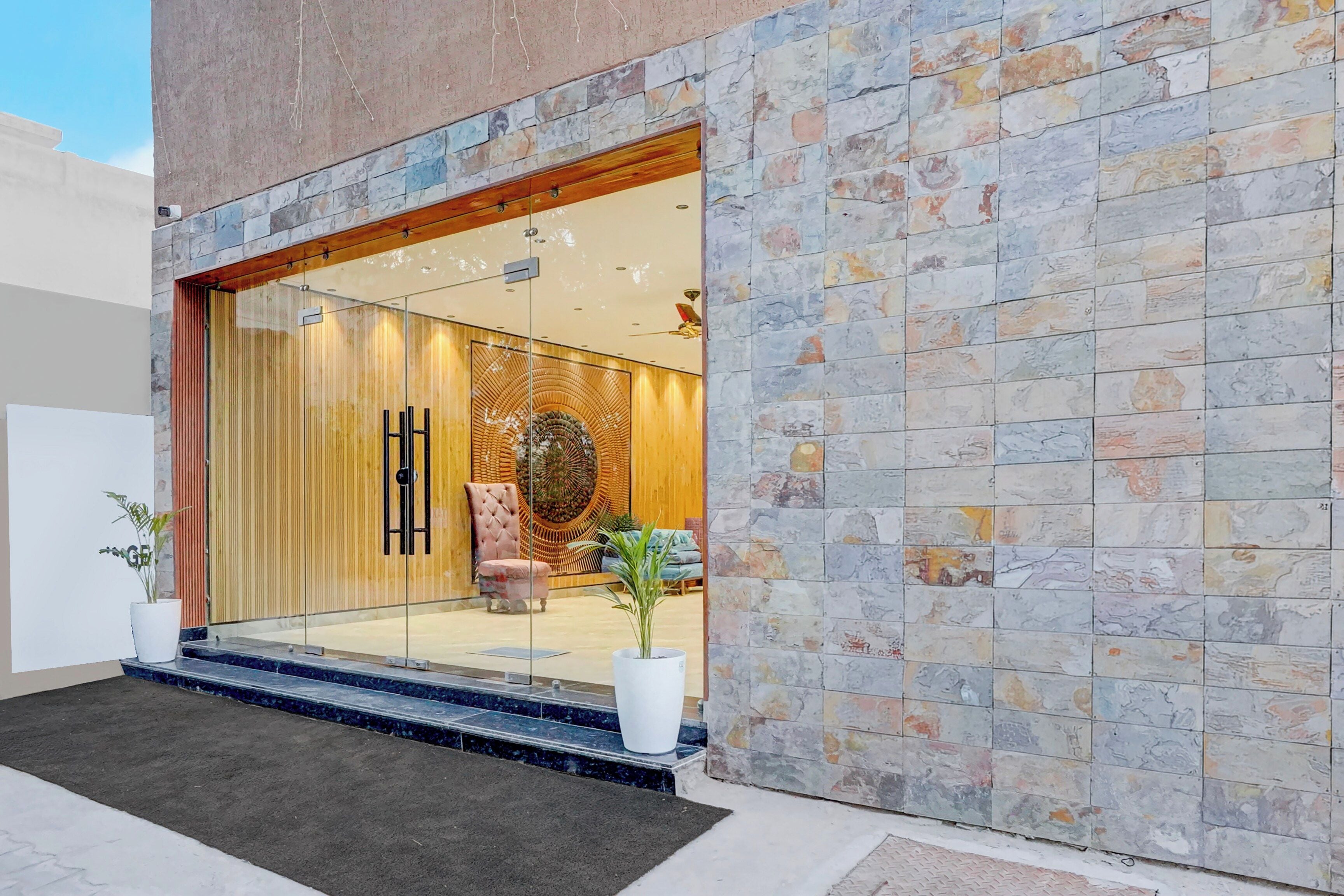 Una entrada moderna a un edificio con fachada de piedra, puerta de vidrio y un área de descanso en el interior.
