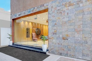 Una entrada moderna a un edificio con fachada de piedra, puerta de vidrio y un área de descanso en el interior.