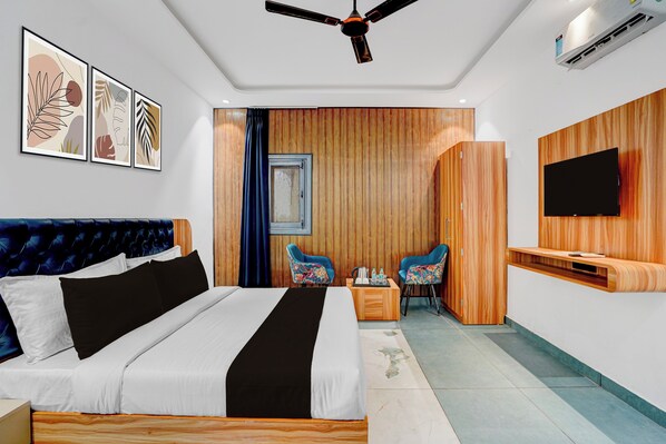 Habitación de hotel con cama, escritorio con sillas, televisor de pantalla plana y obras de arte en la pared.