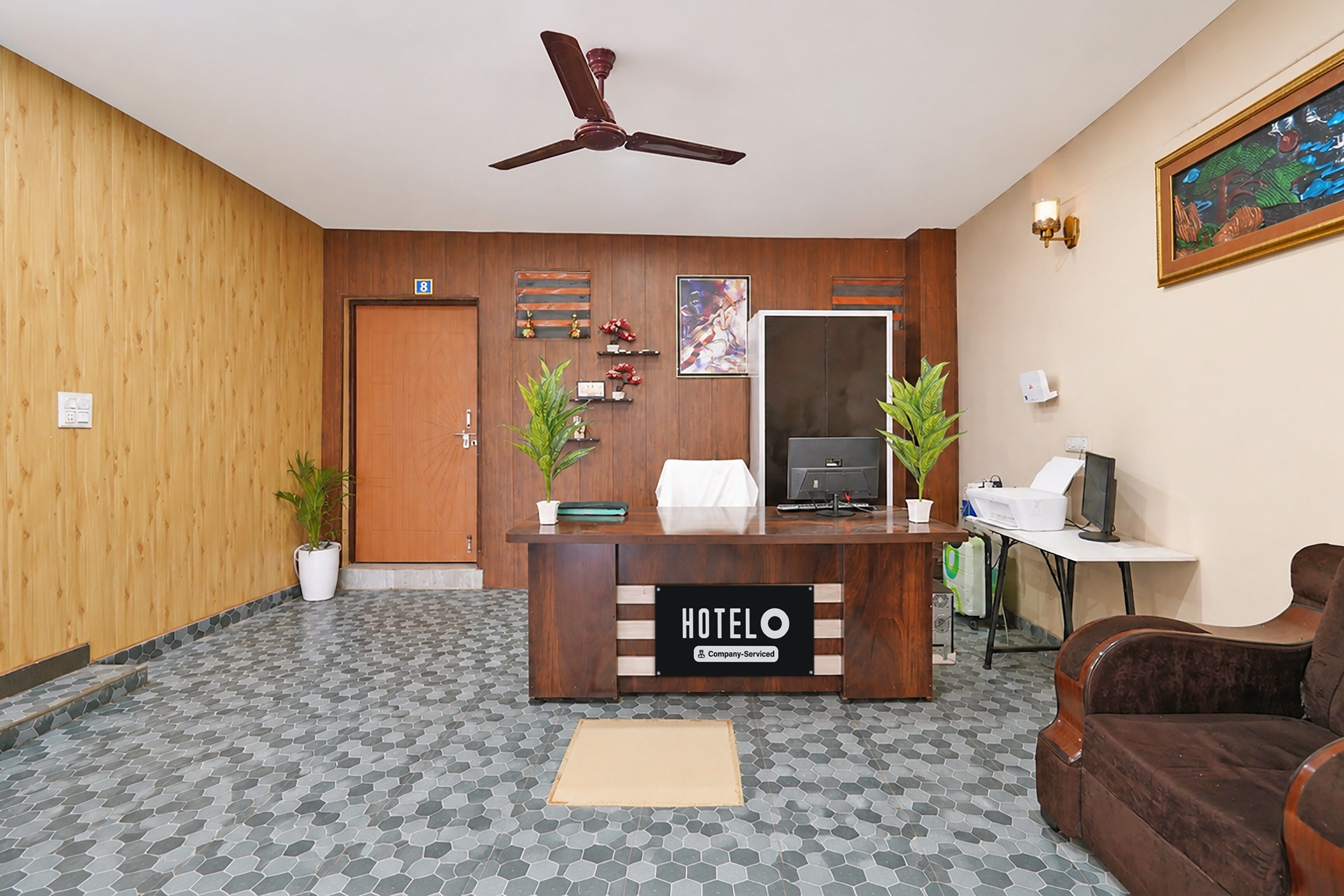 Ein Hotel-Empfangsbereich mit einem Holzbüro, einem Deckenventilator, einem großen Gemälde und einer Rezeption.