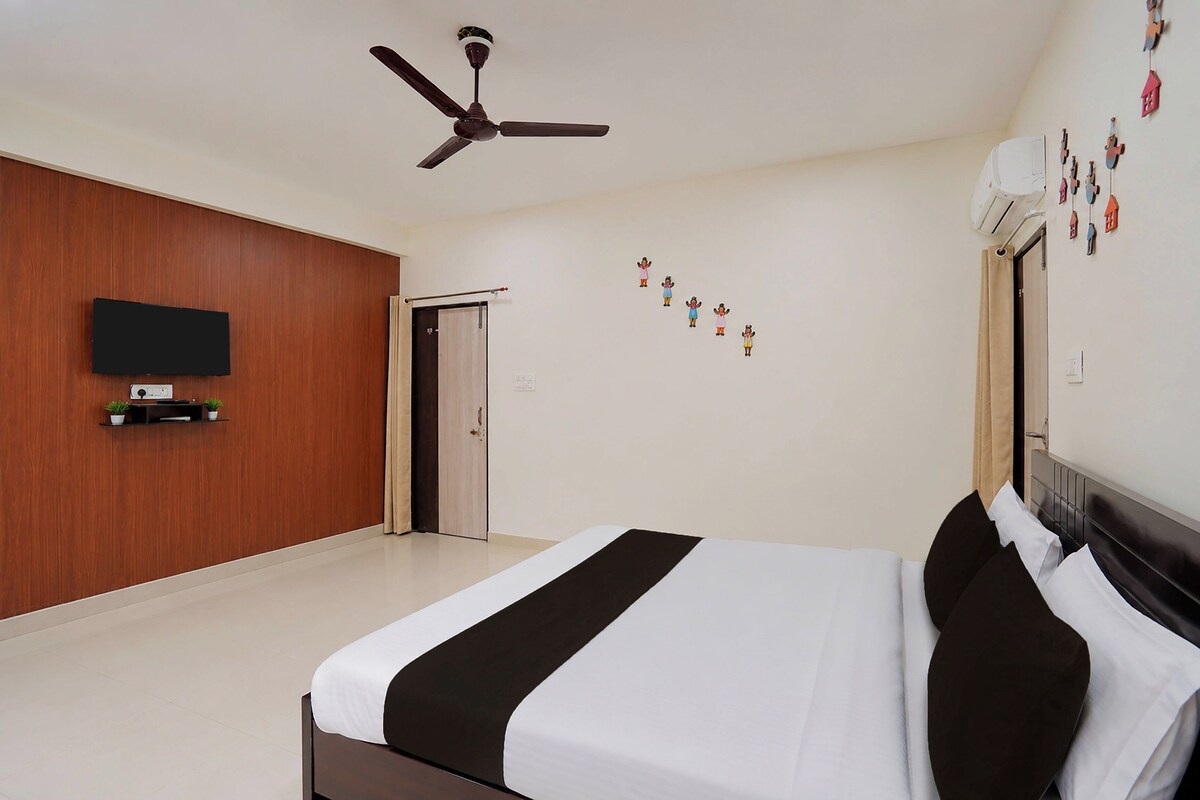 A hotel room with a bed, a ceiling fan, a TV mounted on the wall, and a door leading to another room.