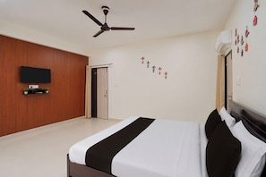 Una habitació d'hotel amb un llit, un ventilador de sostre, un televisor fixat a la paret i una porta que condueix a una altra habitació.