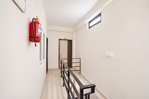 Un passadís amb un extintor fixat a la paret, una porta amb el símbol de número i una finestra amb un respirador.