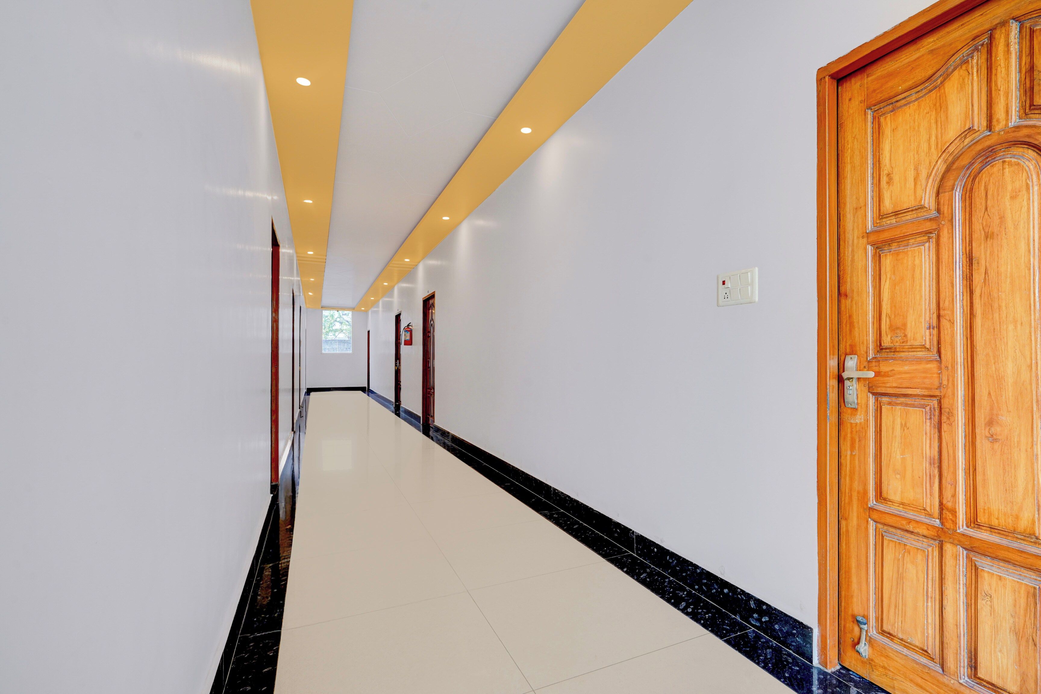 A hallway with a wooden door on the right, white walls, and a tiled floor.