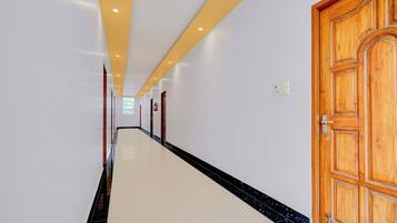 A hallway with a wooden door on the right, white walls, and a tiled floor.