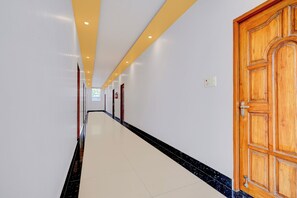 A hallway with a wooden door on the right, white walls, and a tiled floor. - Townhouse Oak Phase 13 Varanasi (Varanasi)