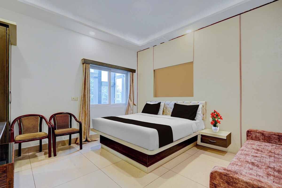 Habitación de hotel con cama, dos sillas, una mesita de noche, una pequeña mesa y una ventana con cortinas.