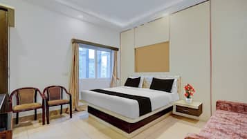 A hotel room with a bed, two chairs, a nightstand, a small table, and a window with curtains.