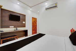 Habitación de hotel con cama, televisor montado en la pared, puerta de madera y unidad de aire acondicionado.