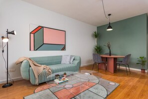 A living room with a teal sofa, a coffee table, a dining area with a table and chairs, a pendant light, and a wall-mounted abstract painting. - Saba Mar Mikhael by Stayinn (Beirut)
