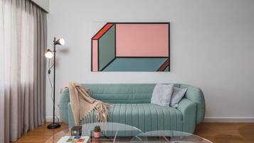 Una habitación con un sofá color turquesa, una mesa de centro de vidrio, una lámpara y una obra de arte geométrica en la pared.