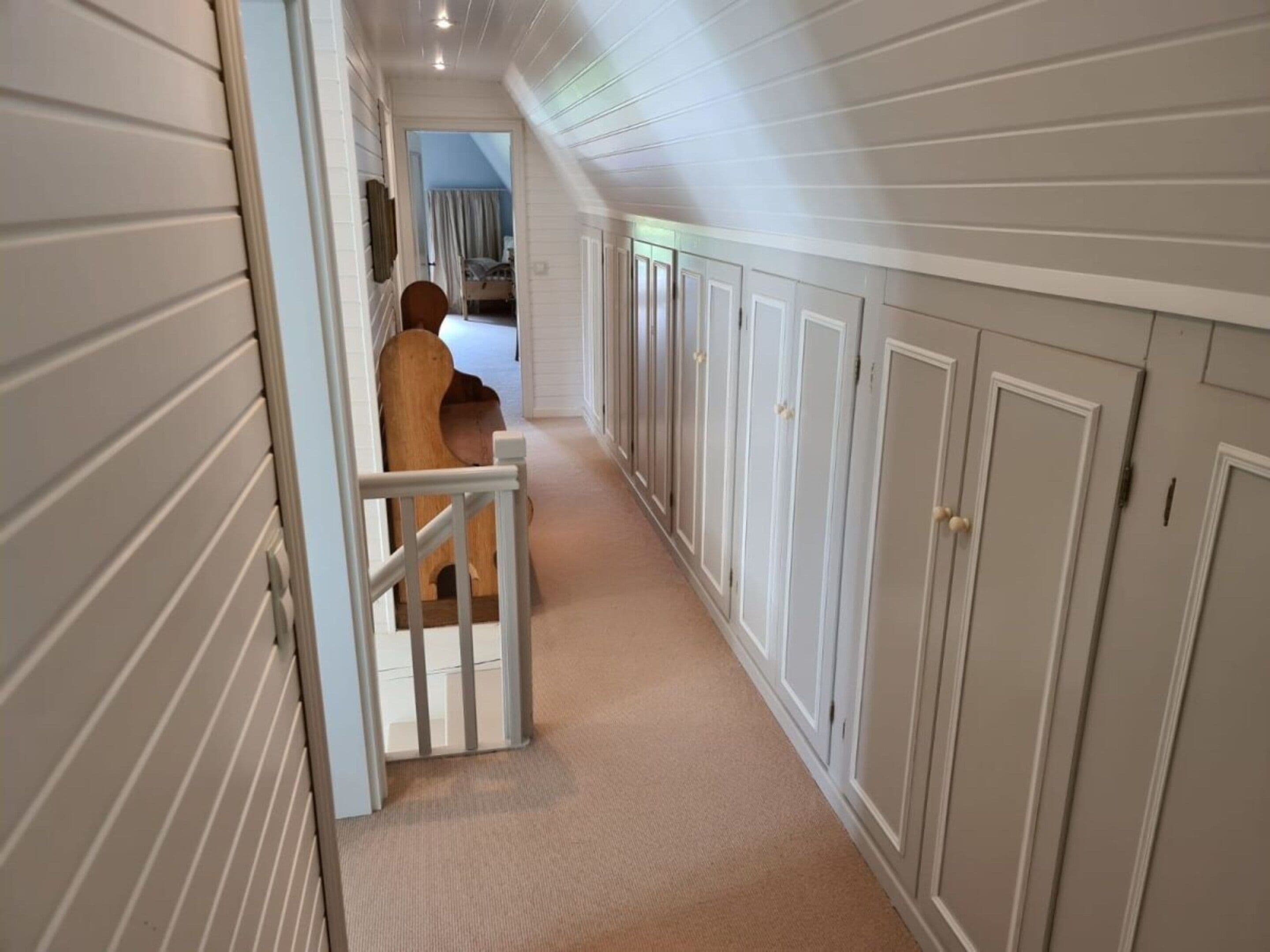 A hallway with a wooden chair, a white door, and a closet with multiple doors.
