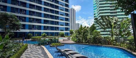 A swimming pool with lounge chairs, surrounded by greenery and modern buildings.