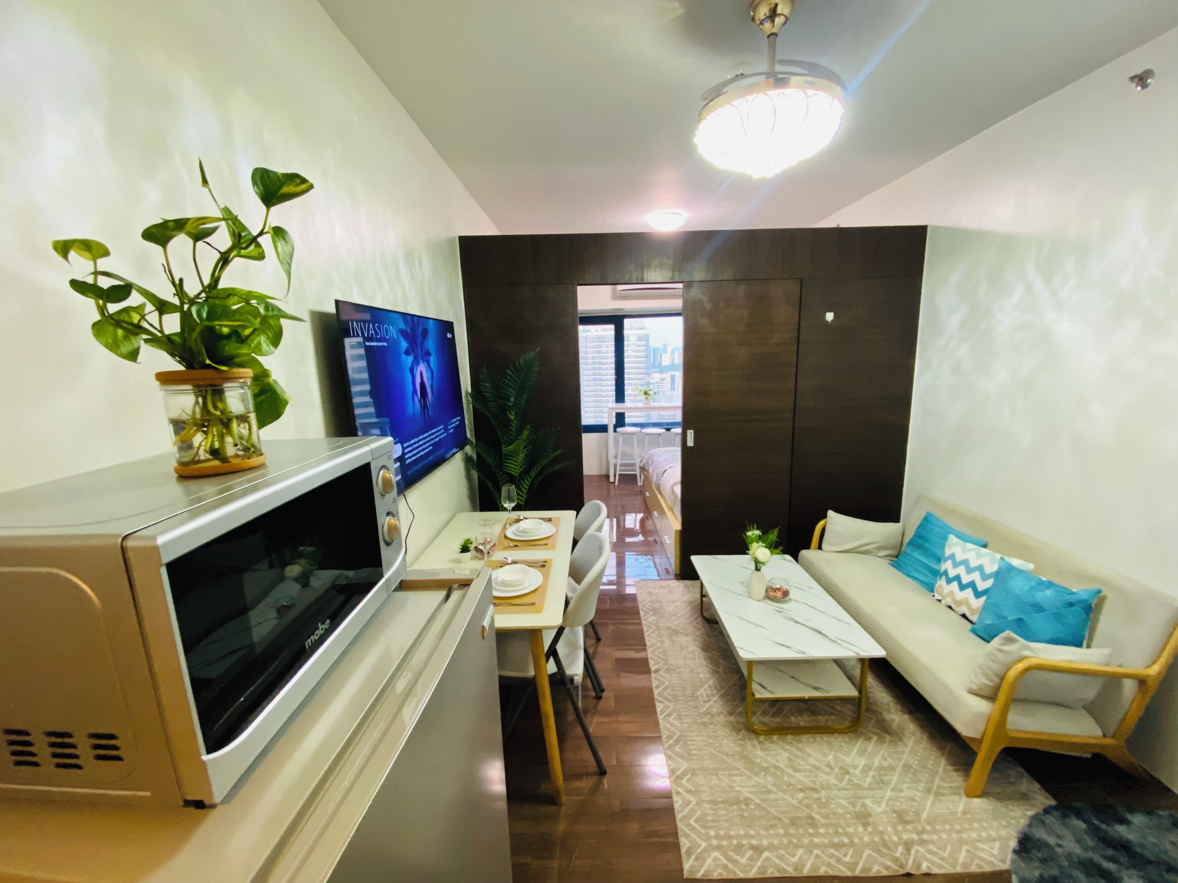 A modern living room with a flat-screen TV, a microwave, a dining table with chairs, a sofa, and a coffee table.