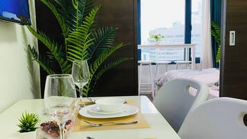 Habitación de hotel con una mesa de comedor para dos personas, una planta en maceta y vistas de la ciudad a través de la ventana.