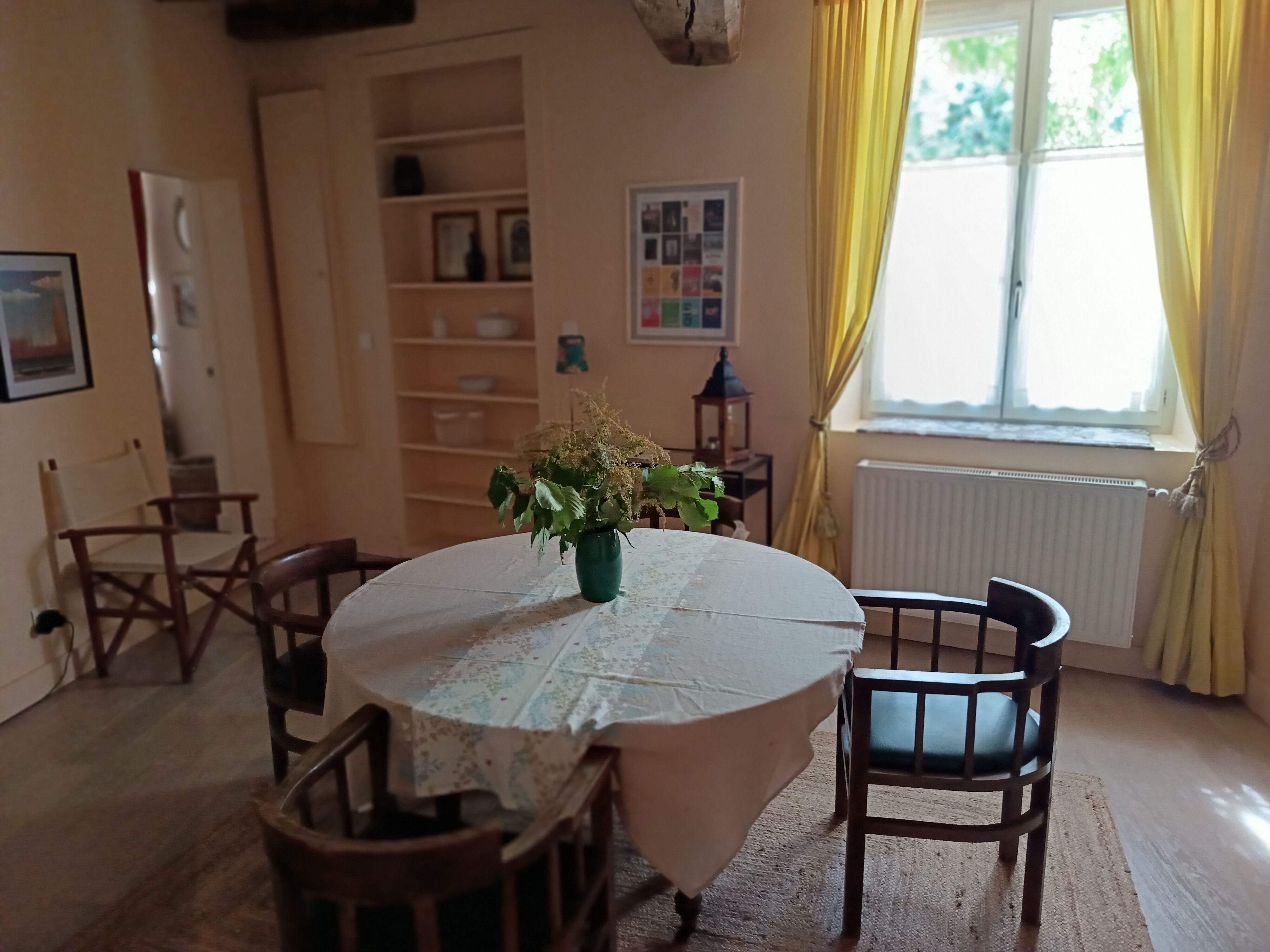 Un coin repas avec une table ronde, des chaises, un arrangement floral en guise de décoration centrale et une fenêtre avec des rideaux.