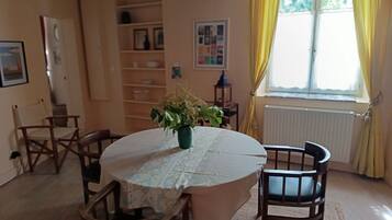 Un coin repas avec une table ronde, des chaises, un arrangement floral en guise de décoration centrale et une fenêtre avec des rideaux.