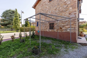 A stone building with a metal structure in front, a paved road, and a grassy area with potted plants. - A cozy and elegant 60-square-meter apartment spread over two floors, ideal for three guests (please note: no elevator; there are internal and external steps). This independent townhouse, located within a courtyard, is situated in the San Concordio distri (Lucca)