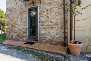 Edifici de pedra amb una reixa metàl·lica, una planta en test i una cadira groga a l'exterior.