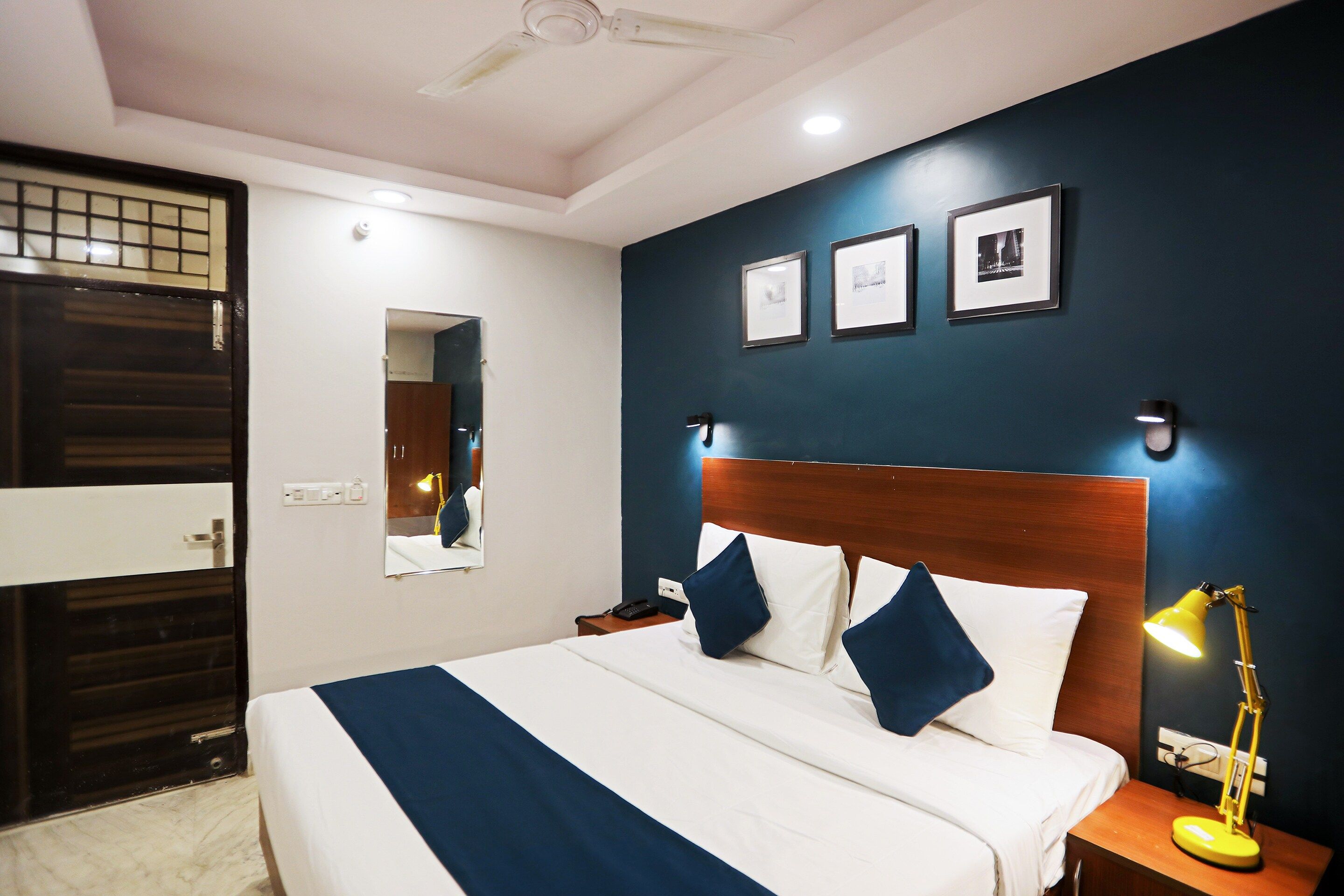 Una habitación de hotel con una cama grande, mesitas de noche, un espejo y cuadros en la pared.