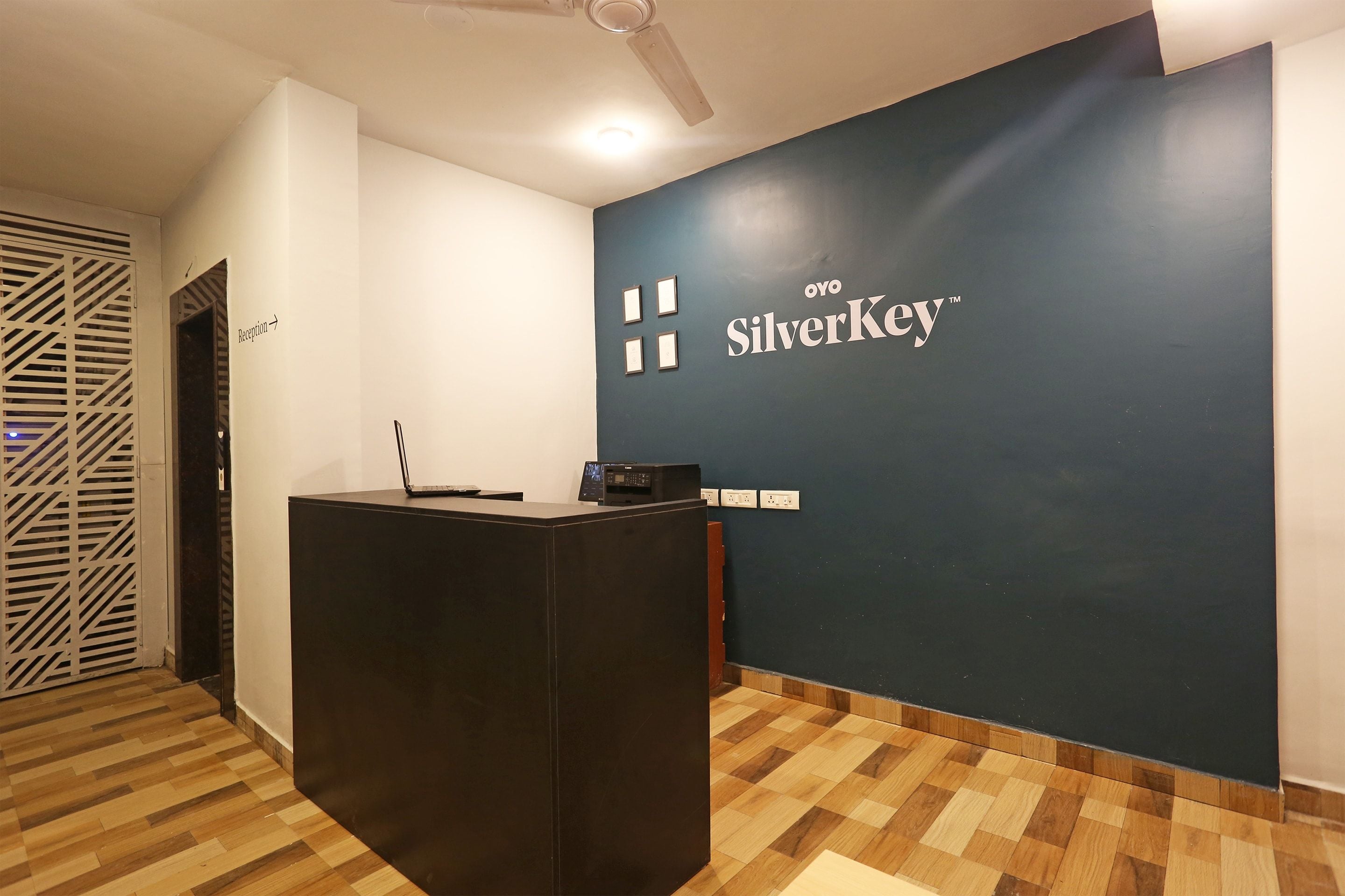 Una reception con un cartello che riporta 'Oyo SilverKey' in un'accogliente hall moderna, con pavimento in legno e ventilatore a soffitto.