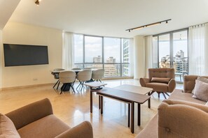 A modern living room with a flat-screen TV, comfortable seating, a dining area, and large windows offering a city view. - Sodeco Ashrafieh by Stayinn (Beirut)