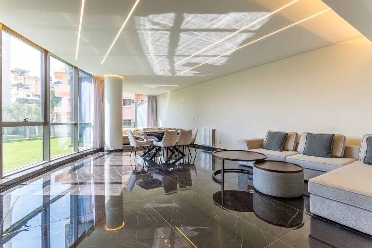 A modern hotel lobby with a glass partition, a dining area, and a seating area with sofas and tables.