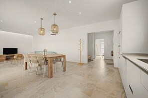 Une cuisine moderne avec des meubles blancs, un coin repas doté d’une table et de chaises en bois, et un éclairage suspendu.