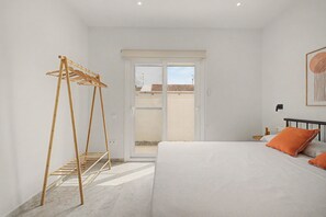A bedroom with a bed, a wooden drying rack, a window with a view of buildings, and a wall-mounted artwork. - Lo Freixer Holiday Home — pool, tranquility, and the river steps away in Deltebre (Deltebre)