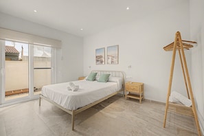 A bedroom with a bed, a nightstand, a wooden hanger, and a view through a sliding door. - Holiday Home 'Lo Tamariu' with Private Pool, Wi-Fi and Air Conditioning (Deltebre)