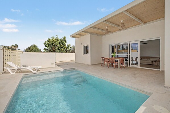 A swimming pool with lounge chairs and a dining area with outdoor furniture. - Holiday Home 'Lo Tamariu' with Private Pool, Wi-Fi and Air Conditioning (Deltebre)