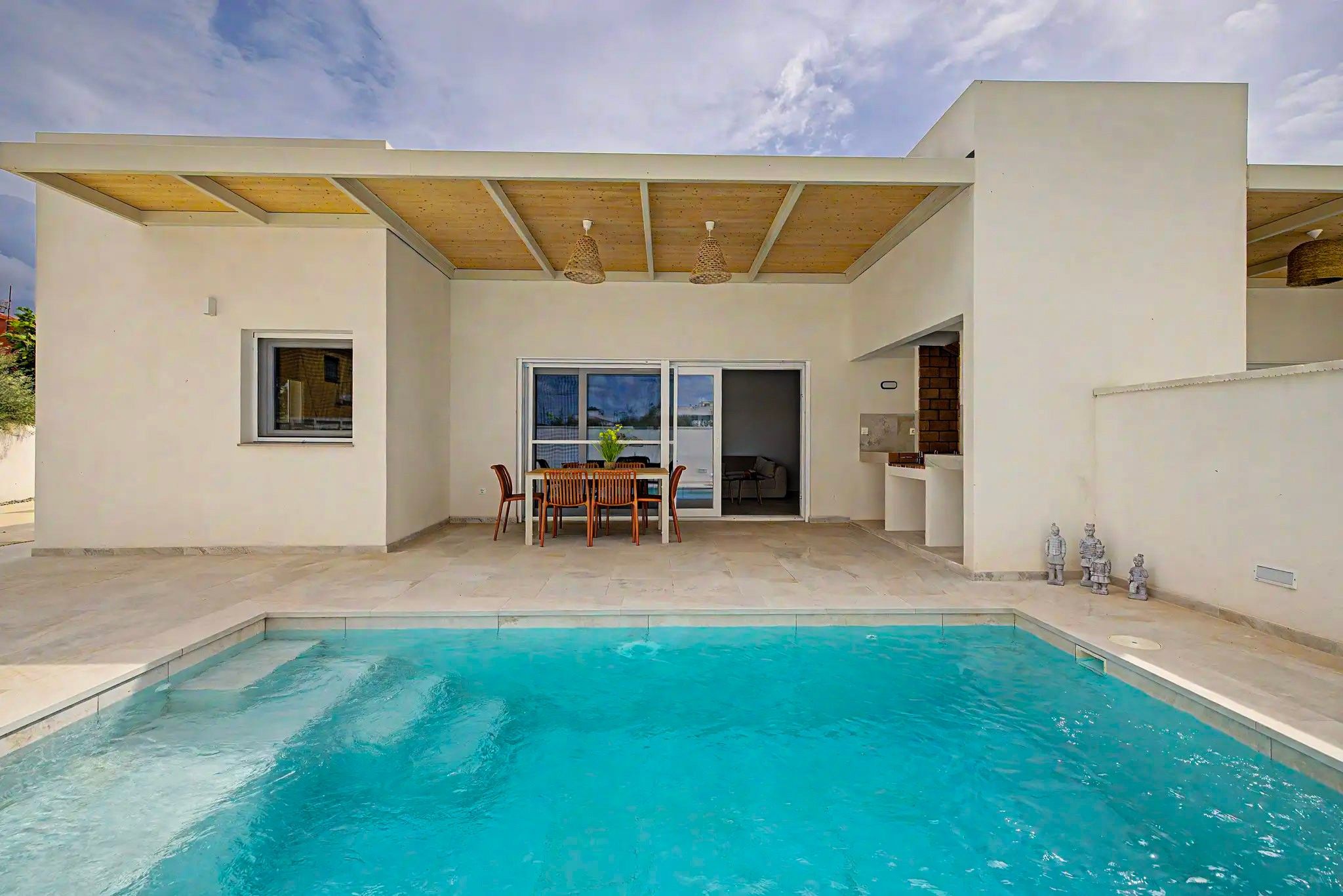 Una piscina con zona de patio, una mesa con sillas y vistas al cielo.