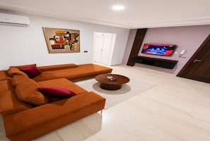 A modern living room with a sectional sofa, a coffee table, a flat-screen TV, and a painting on the wall. - Cozy & Bright Aouina Apartment (Site archéologique de Carthage)