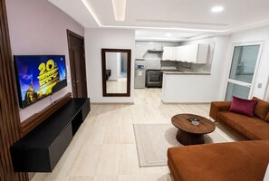 Un saló modern amb televisió plana, un sofà, una taula de centre i una cuina al fons.