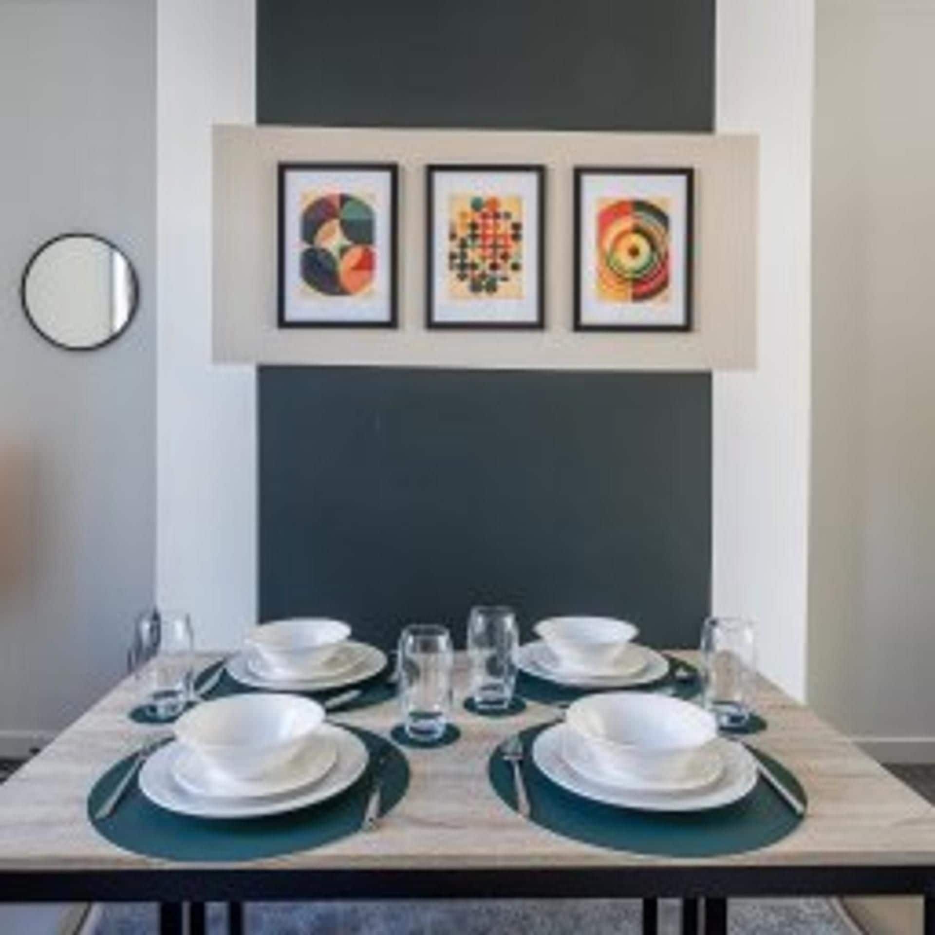 Ein Essbereich mit einem Tisch für vier Personen, Kunstwerken darüber und einem runden Spiegel an der Wand.